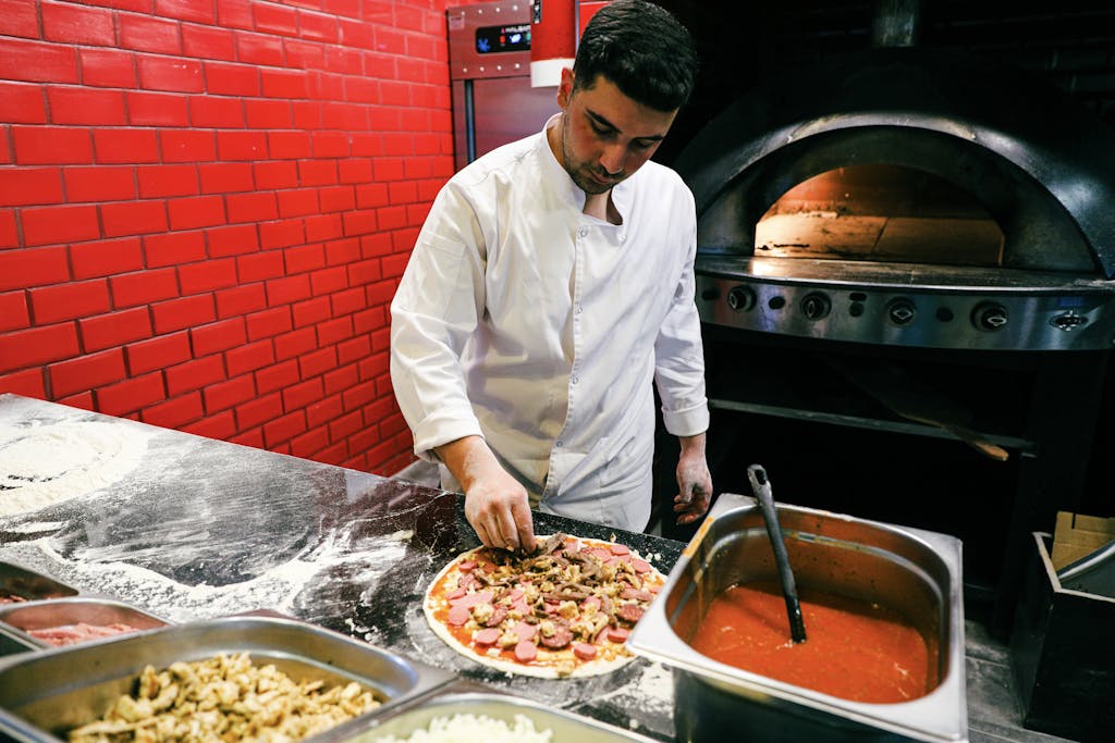 Chef in white uniform preparing pizza in a brick oven kitchen. Italian cuisine and culinary art.